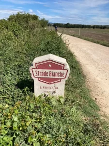 Een iconische Strade Bianche mijlpaal langs een stoffige gravelweg in Toscane tijdens een fietsvakantie.