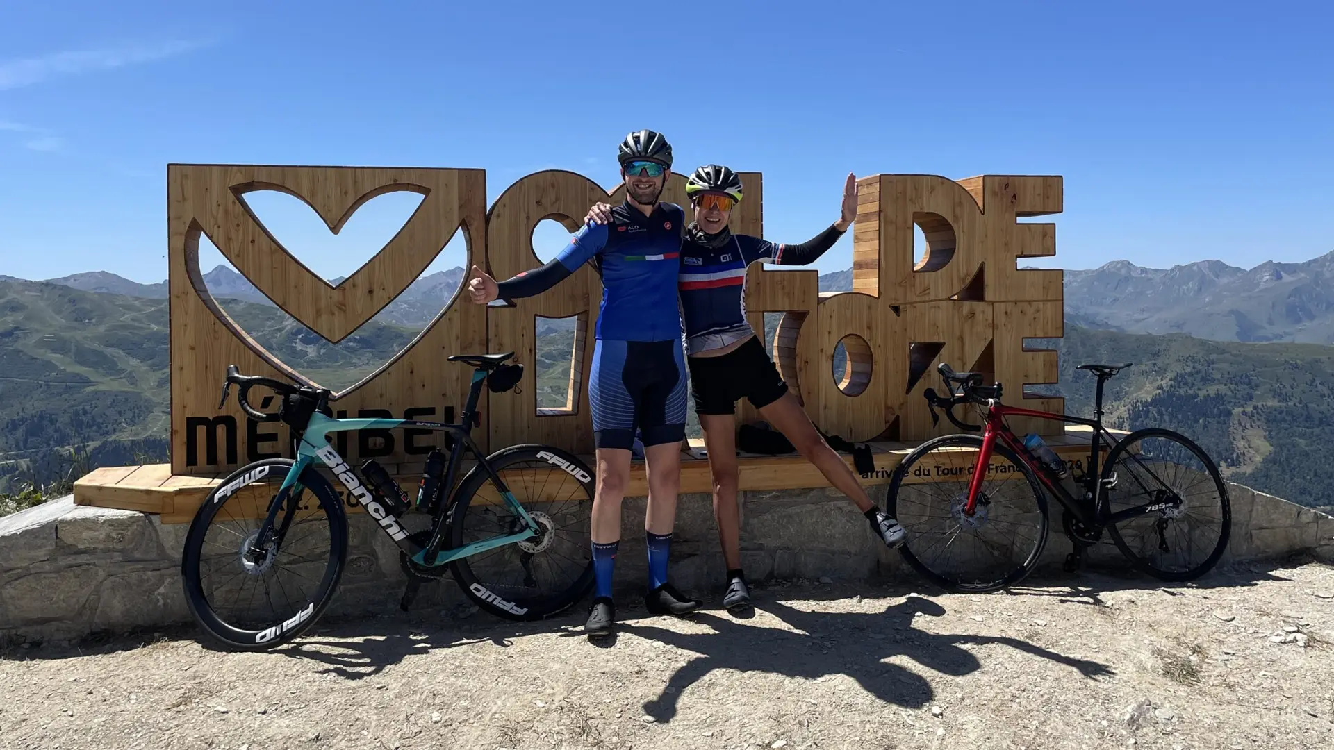 Twee wielrenners met racefietsen bij het Col de la Loze monument in de Franse Alpen